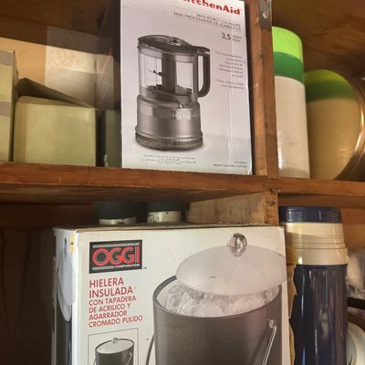 Sale Photo Thumbnail #96: KitchenAid 3.5-cup mini food processor boxed set alongside an Oggi insulated ice bucket box stored on wooden shelving.