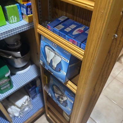 Sale Photo Thumbnail #240: Wooden pantry cabinet shelves stocked with household goods, light bulbs, and food storage supplies.