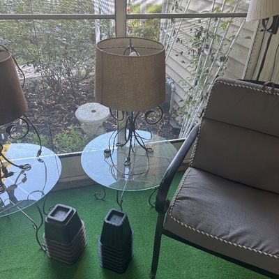 Sale Photo Thumbnail #9: Pair of wrought iron table lamps with glass top integrated side tables and tan fabric shades, shown on a sunporch alongside outdoor seating and furniture risers.