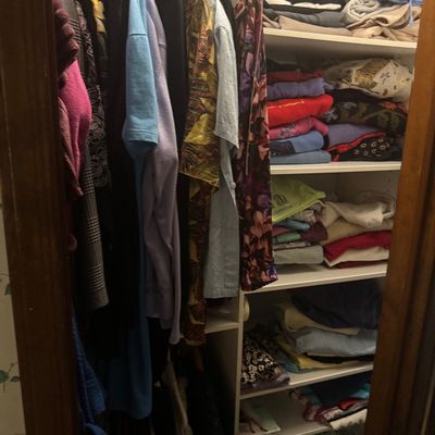 Sale Photo Thumbnail #22: A closet filled with hanging men's and women's clothing alongside stacked shirts and sweaters on white organizer shelves.