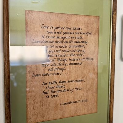 Framed calligraphic art piece featuring the biblical passage 1 Corinthians 13:4-13 on parchment-style paper with a green mat and wooden...