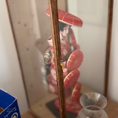 Traditional Japanese geisha doll dressed in a red kimono with red parasols, enclosed in a wooden framed glass display case.