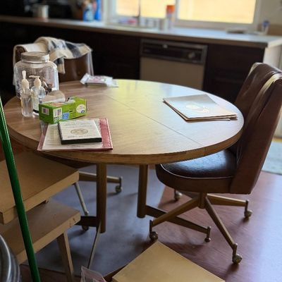 Mid-century wooden round kitchen table set with rolling vinyl chairs.