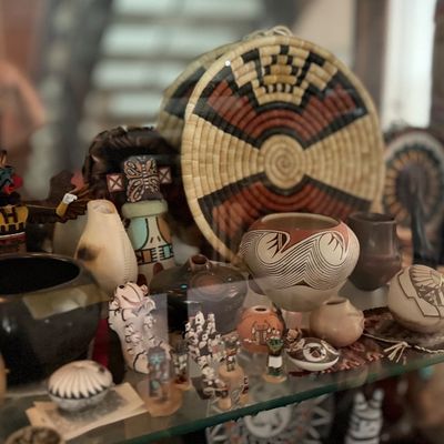 Display case filled with Southwestern Indigenous art objects, including woven baskets, pottery pieces, and kachina figures.