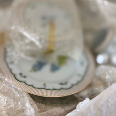 Sale Photo Thumbnail #121: Porcelain saucer with floral motif and gilded rim packed in protective bubble wrap.