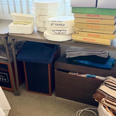 Sale Photo Thumbnail #135: Folding display tables stacked with Belleek porcelain collector boxes, audio speakers, and textiles.
