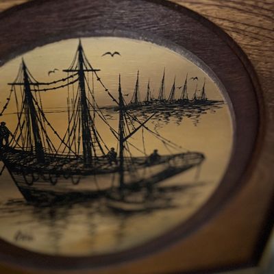 Nautical-themed circular wood inlay featuring a detail of a sailing ship set within a faux-wood grain panel.