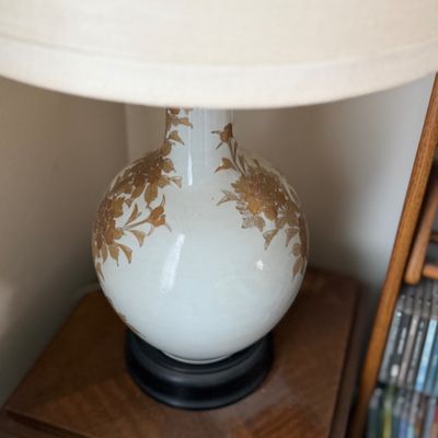Vintage ceramic table lamp featuring a bulbous white base with gold floral accents and a large neutral fabric shade.