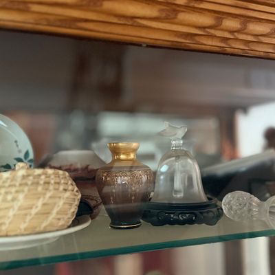 Collection of decorative trinkets and glassware, including a mini woven basket, a small gilded ceramic vase, a glass bell, and a floral...
