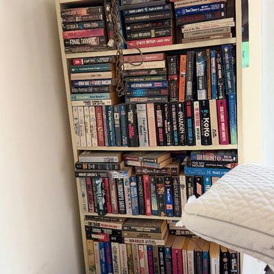 Sale Photo Thumbnail #119: Tall white wooden bookcase filled with a large collection of paperback and hardcover fiction books.