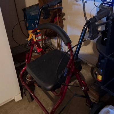 Sale Photo Thumbnail #164: Red four-wheeled rollator walker with a padded black seat and backrest support.