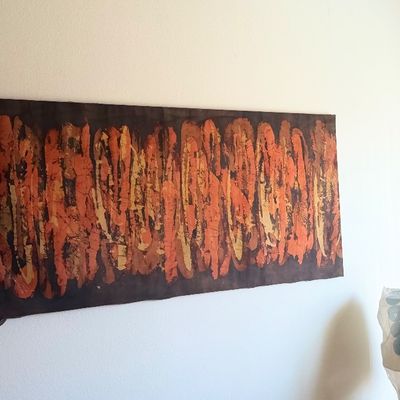 Large horizontal abstract batik fabric wall hanging featuring warm orange, yellow, and brown tones.