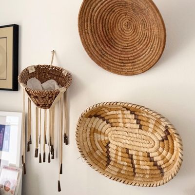 Sale Photo Thumbnail #148: Collection of three woven wall baskets, including a round coiled tray, a geometric patterned oval tray, and a hanging basket with fringe detailing.