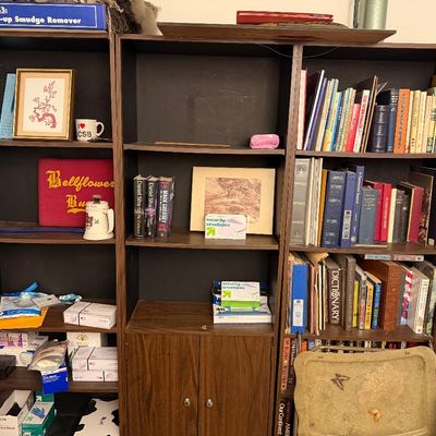 Set of dark laminate wooden bookcases filled with books, office supplies, framed artwork, and miscellany.