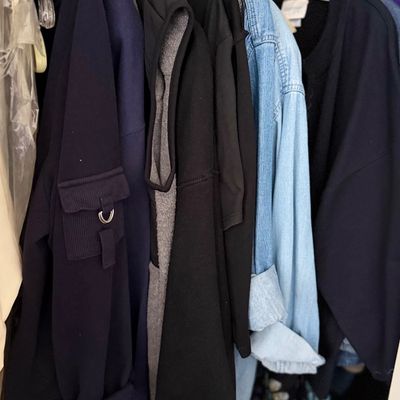 Selection of men's and women's casual clothing hanging in a closet, including dark hoodies, vests, and a light denim...