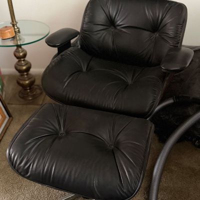 Mid-century modern style black tufted leather lounge chair with matching ottoman on a metal base.