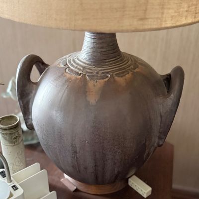 Mid-century studio pottery table lamp featuring a rounded body with integrated handles and a textured neutral-toned shade.