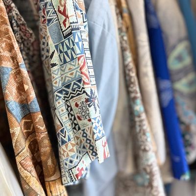 Sale Photo Thumbnail #110: Men's Hawaiian button-up shirt featuring a light blue, geometric mosaic and tropical pattern hanging in a closet.