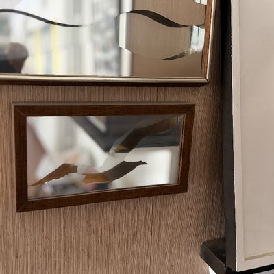 Framed mirror with an etched or painted flying bird design mounted on a wood-grain panel.