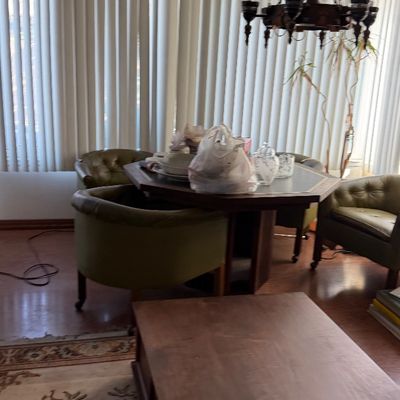 Sale Photo Thumbnail #176: Mid-century wooden dining set featuring an octagonal table with green vinyl tufted barrel armchairs, accompanied by a hanging wrought iron chandelier.