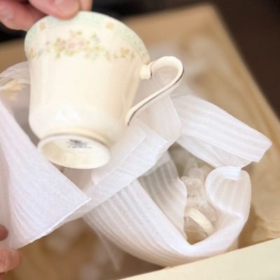Sale Photo Thumbnail #125: Fine china teacup with pastel floral trim and platinum accenting, being unpacked from protective foam wrapping.