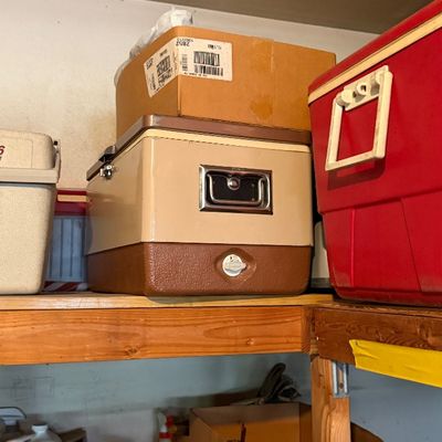 Sale Photo Thumbnail #169: Vintage metal coolers, including a tan and brown retro model and a large red cooler, displayed on garage storage shelving.