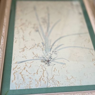 Framed Asian floral artwork depicting a minimalistic flower arrangement in a tall vase, featuring a green mat and a decorative...