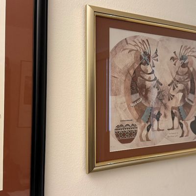 Framed Southwestern-style art print depicting two Kokopelli figures and pottery, set in a gold metal frame.