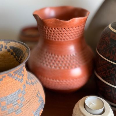 Red terracotta pottery vase with geometric incised textured bands and a scalloped rim.