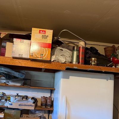 Sale Photo Thumbnail #166: White top-freezer refrigerator positioned under heavy-duty wooden garage storage shelving loaded with household items, boxes, and vintage thermoses.