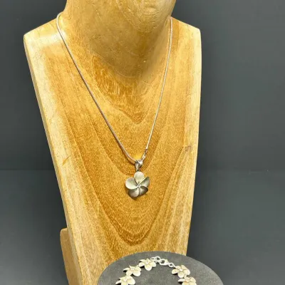 Sale Photo Thumbnail #88: Hawaiian-style sterling silver plumeria jewelry set, including a pendant necklace, matching link bracelet, and stud earrings displayed on a wooden mannequin bust.