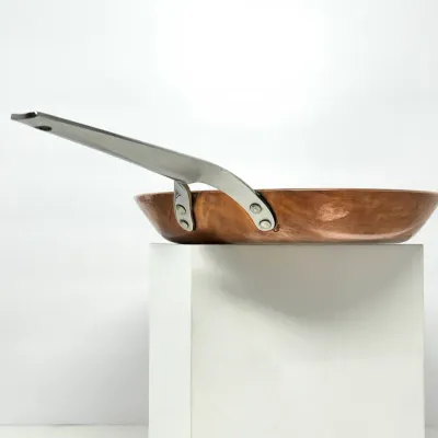 Sale Photo Thumbnail #211: Polished copper frying pan featuring a riveted stainless steel handle, displayed on a white riser.