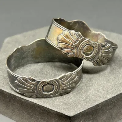 Sale Photo Thumbnail #164: Pair of vintage tarnished silver-plated napkin rings featuring ornate fan and shell motif relief designs.