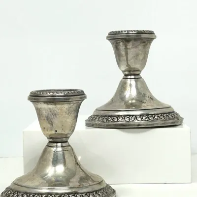 Sale Photo Thumbnail #113: Pair of vintage silver-plated low candlestick holders featuring embossed floral trim along the rims and bases, displaying minor tarnishing.