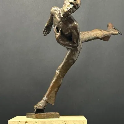 Sale Photo Thumbnail #34: Bronze sculpture of a male figure skater in motion, mounted on a light-colored marble or stone base.