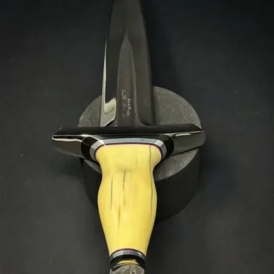 Sale Photo Thumbnail #199: Custom double-edged dagger featuring a polished dark blade, an engraved guard, and a carved ivory or bone handle with red accent spacers.