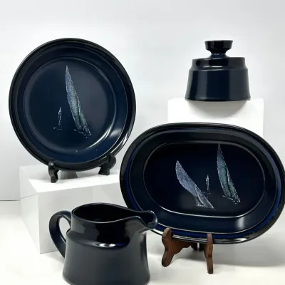 Sale Photo Thumbnail #104: Four-piece vintage dark blue ceramic tableware set featuring a sailboat design, including a plate, platter, creamer, and covered vessel.