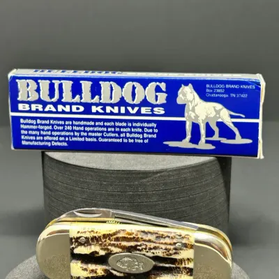 Sale Photo Thumbnail #175: Bulldog Brand pocket knife featuring a stag handle with an inlaid fish shield, displayed with its original blue and white box.