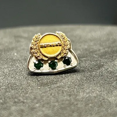 Sale Photo Thumbnail #170: Vintage Mother's service award lapel pin featuring three set green gemstones below a gold-tone laurel wreath crest.
