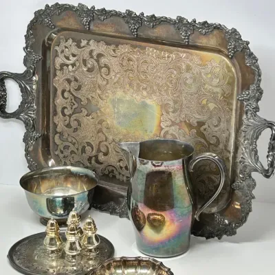 Sale Photo Thumbnail #194: Collection of silver-plated tableware featuring a large ornate handles tray with grape motif border, a water pitcher, salt and pepper shakers, and small serving bowls showing vintage patina and tarnish.