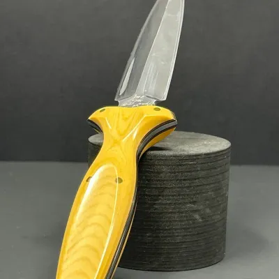Sale Photo Thumbnail #73: Custom fixed-blade boot knife featuring a polished double-edge dagger blade, a yellow composite or Micarta handle with brass pins, and a lanyard hole.