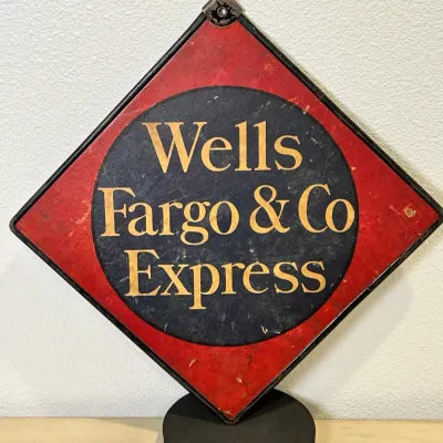 Sale Photo Thumbnail #141: Vintage Wells Fargo & Co. Express diamond-shaped metal sign with red, black, and gold lettering, mounted on a display base.