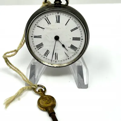 Sale Photo Thumbnail #108: Antique key-wind pocket watch featuring a white enamel dial with Roman numerals, accompanied by a brass winding key attached with twine.