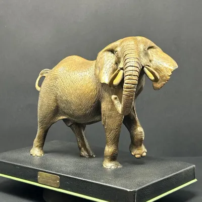 Sale Photo Thumbnail #140: Detailed bronze sculpture of a walking elephant mounted on a black faux-leather plinth base with a brass nameplate.