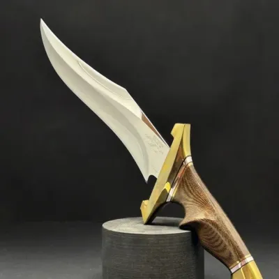 Sale Photo Thumbnail #12: Custom fixed-blade Bowie-style knife with polished steel clip-point blade, brass guard and pommel, and contoured wood handle, displayed on a cylindrical stand.