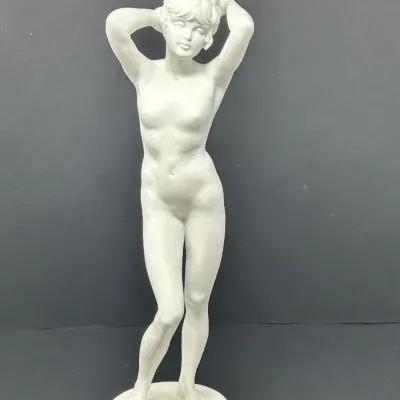 Sale Photo Thumbnail #64: White porcelain or bisque figure of a standing female nude posing on a round pedestal base.