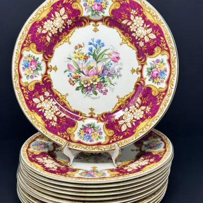 Sale Photo Thumbnail #187: Stack of vintage porcelain dinner plates featuring a rich magenta and gilt scrollwork border surrounding a center floral bouquet motif.