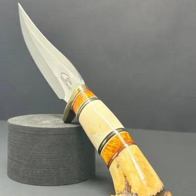 Sale Photo Thumbnail #163: Custom fixed-blade hunting knife by Colin Cox, featuring a polished steel blade, a brass guard, and a composite handle made of stag antler, bone, and burl wood spacers.