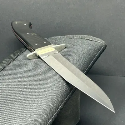 Sale Photo Thumbnail #31: Fixed-blade hunting knife with a black Micarta handle and silver guard, displayed resting on a black padded zippered pouch.