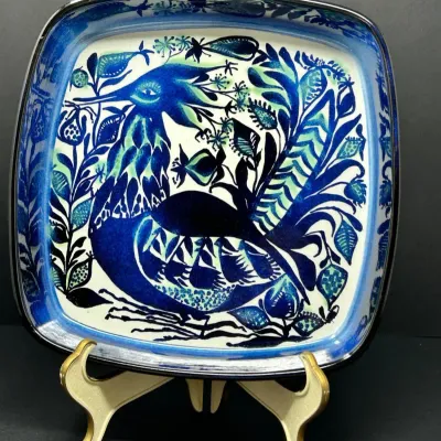 Sale Photo Thumbnail #51: Mid-century modern glazed ceramic dish featuring a stylized blue and green peacock or bird motif, displayed on a gold-tone easel stand.